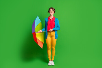 Full length body size photo of positive girl in eyewear holding colorful umbrella smiling isolated on vivid green color background © deagreez