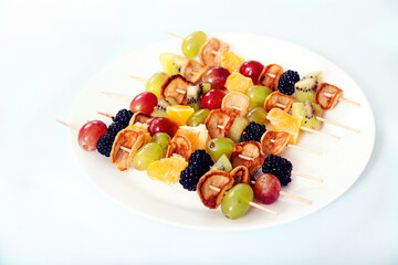 Dessert on skewers from minipuncakes, blackberries, vgrada and kiwi on a plate on a light concrete background.
