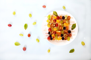 Dessert on skewers from minipuncakes, blackberries, vgrada and kiwi on a plate on a light concrete background.