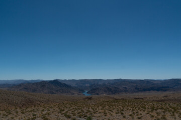 Fototapeta na wymiar A river can be seen far off in between some mountains and canyons at the border between Arizona and Nevada. The landscape signals proximity close to a famous dam. 