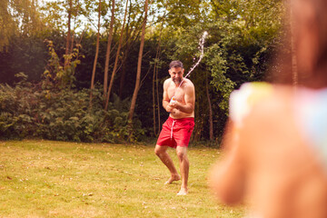 Fototapeta premium Father And Son Wearing Swimming Costumes Having Water Fight With Water Pistols In Summer Garden