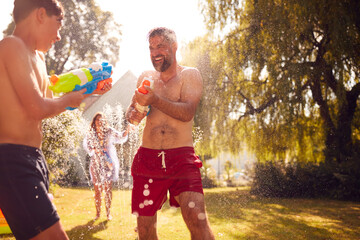 Obraz premium Family Wearing Swimming Costumes Having Water Fight With Water Pistols In Summer Garden