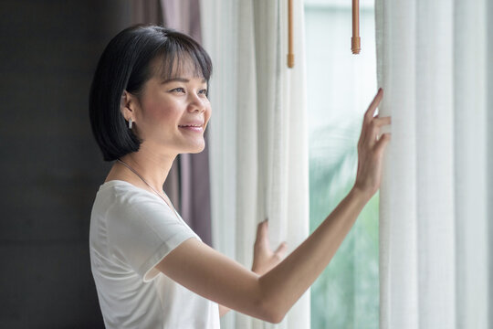 Asian woman smile and looking at outdoor with curtain at a room in the hotel