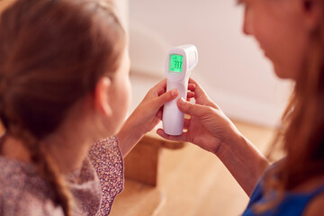 Close Up Of Mother Checking Daughters Temperature At Home Using Contactless Digital Thermometer