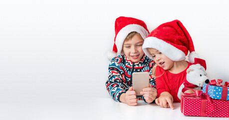 Online christmas greetings. Brother and sister in Santa hats smile and talking on the phone.