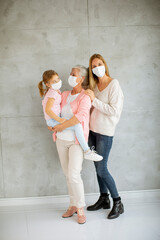 Fototapeta na wymiar Senior woman, adult woman and little girl, three generations with protective facial masks at home