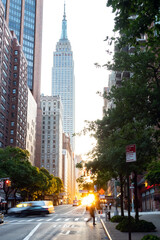 Busy intersection on 42nd Street in Midtown Manhattan with sunset shining between the buildings of...