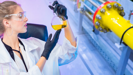 Chemist at the company. Female laboratory assistant examines a yellow chemical liquid in a test...