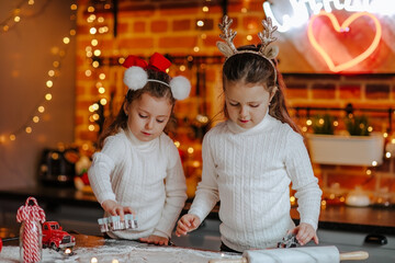 Fototapeta na wymiar Girls in sweaters making cookies on the kitchen with Christmas background.