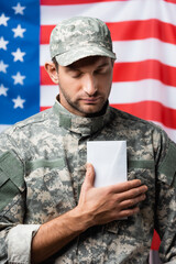patriotic military man in uniform and cap holding envelope near american flag on blurred background