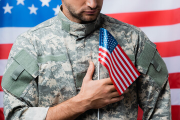 cropped view of patriotic military man in uniform holding small american flag on blurred background