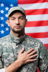 patriotic military man in uniform pledging allegiance near american flag on blurred background