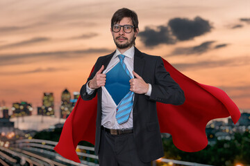 Businessman in suit as superhero is opening his shirt. City in background.