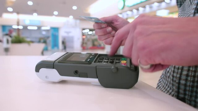 A man makes a payment by credit card at a store. Inserts a card into the terminal, enters a pin. Cashless settlement is the rule of social distance.