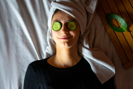 Woman lying in bed with two cucumber slices on her eyes.