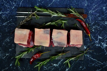 Raw meat ribs on a black stone plate, decorated with green sprigs of rosemary, Dark granite background. Raw Organic Beef Short Ribs