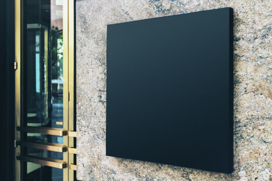 Black square sign with blank space for your logo on the marble wall of a modern shopping center, mockup