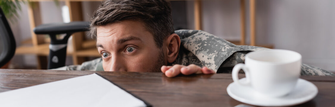 Scared Military Man Hiding Under Desk, Banner