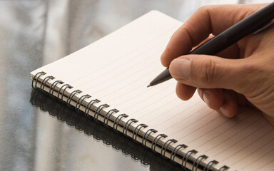 A hand holding a pen.  Hand writing on a notebook.