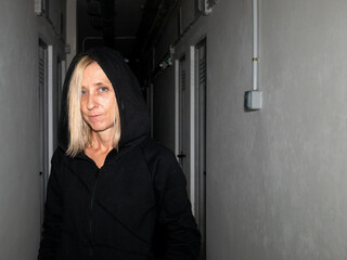 BLOND SPANISH WOMAN DRESSED IN BLACK HOODED COAT, IN THE CORRIDOR OF A BASEMENT WITH A SINIEST LOOK