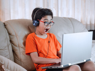 Little boy wearing headphones with shocked and surprised sitting at the table with communication...