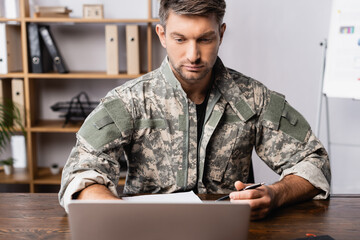 soldier in uniform sitting at desk and using laptop