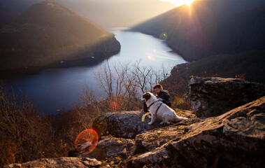 man and his dog sitting on rock enjoying amazing autumn view over lake at sunset