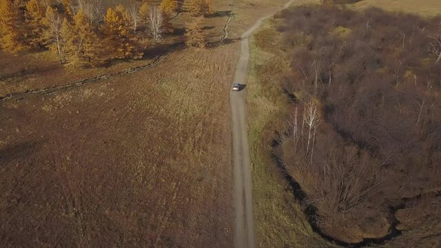 Aerial view shoot. The SUV car quickly drives through the desert area along the mountains and autumn forest, leaving behind a raised dust and a long trail on the gravel. Adventure and off road concept