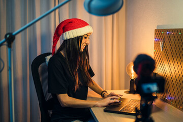 Chica con gorro de papa noel realizando vlog en su cuarto y trabajando en el pc