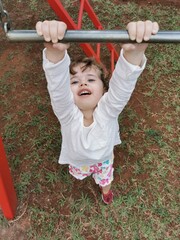 Fototapeta premium Portrait Brazilian Little girl playing hanging on bar at the playground