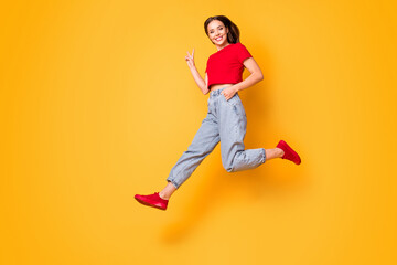 Fototapeta na wymiar Full length photo of cute jumping lady showing v-sign wear red crop top jeans shoes isolated yellow color background