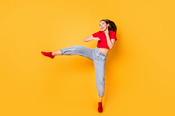 Boxer girl practicing air kicks raise leg jumping high wear red crop top jeans isolated yellow...