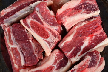 Raw meat ribs on a black silver plate, gray wooden background. Raw Organic Beef Short Ribs