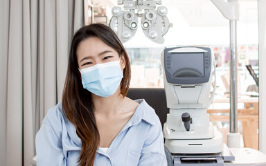 Fototapeta na wymiar Asian woman wearing mask and doing eyes test in optical lab