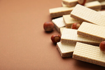 Wafers, cookies and sweets concept with hazelnut, chocolate and vanilla filled wafer stack with raw hazelnuts on a brown background
