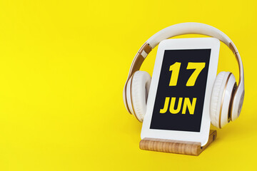 June 17th. Day 17 of month, Calendar date. Stylish headphones and modern tablet on yellow...