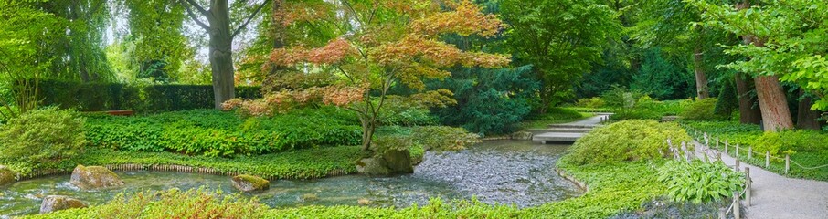Beautiful Japanese garden with a small stream, in panorama format.