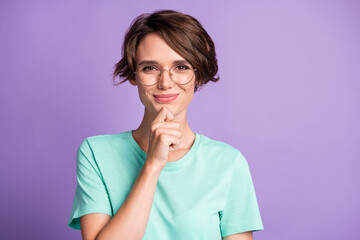 Photo of optimistic cute short brown hairdo girl fist chin wear spectacles blue t-shirt isolated on violet background