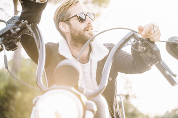 Man smoking with distracted expression while leaning against a handlebar of a motorcycle