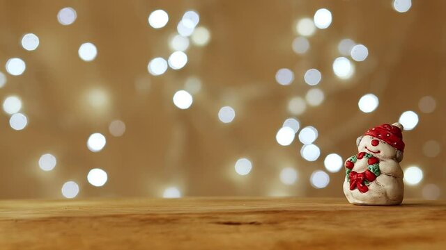 New Year toy snowman stands on a wooden table top on a brown background. Christmas garland sparkles in the background