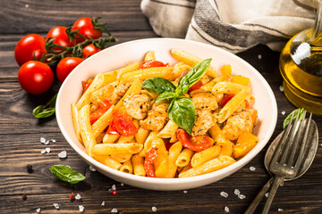 Pasta with chicken and vegetables at wooden table.
