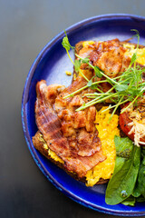 Very bright and healthy breakfast on a plate - bacon, egg, salad, tomato, cheese, a glass of yogurt. Close-up, top view.