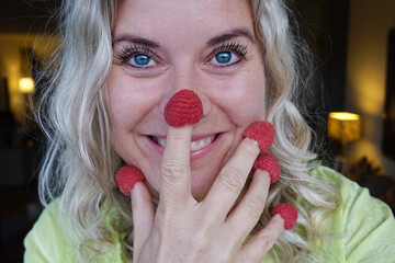 Woman creating a red nose with raspberries on fingers