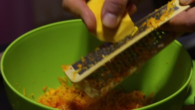 A man is rubbing pieces of pumpkin on a grater. Pumpkin shavings are placed in a container. Close-up shot from the side