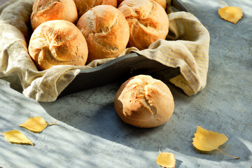 Kaiser, or Vienna buns in bread basket on dark grey background with yellow Autumn leaves.