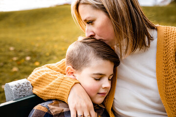 mother consoling child boy in the autumn leaf fall sit on bench