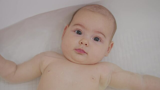 A nice little caucasian newborn baby is funny smiling, lying at the back in the bath. Portrait of a playful and energetic child close-up.