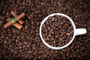 White cup full of coffee beans and cinnamon on a coffee beans background. Coffee mug. 
