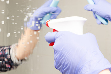 closeup female hands sprinkle cleaning agent on the bathroom mirror and wipe it