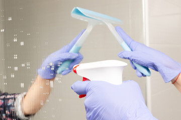closeup female hands sprinkle cleaning agent on the bathroom mirror and wipe it